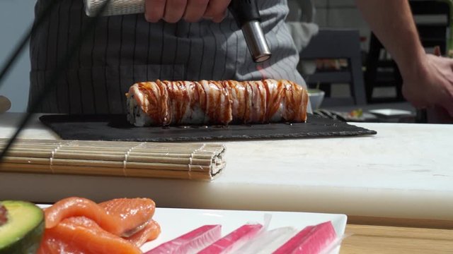 Sushi master prepares sushi in modern style. Chef is blowing fire by blowtorch on salmon Sushi. Fusion cuisine, caramelized salmon on sushi