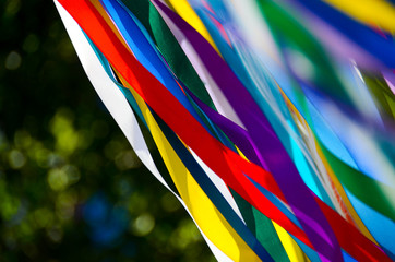 Many multicolored ribbons flutter in the wind in the sun. background
