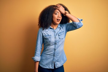 Young beautiful african american woman with afro hair standing over yellow isolated background...