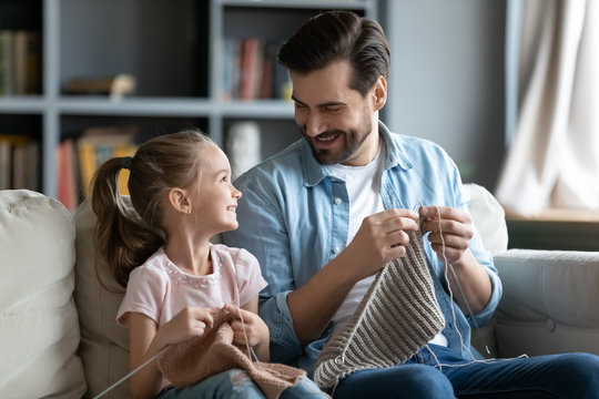 Smiling father and little daughter knitting at home together