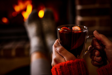 Woman with tasty mulled wine near burning fireplace indoors, closeup