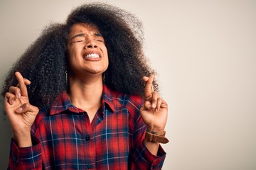 Young beautiful african american woman wearing casual shirt over isolated background gesturing finger crossed smiling with hope and eyes closed. Luck and superstitious concept.