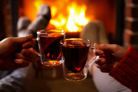 Couple with tasty mulled wine near fireplace indoors, closeup