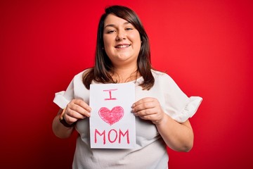 Beautiful brunette plus size woman holding love mom message celebrating mothers day with a happy face standing and smiling with a confident smile showing teeth