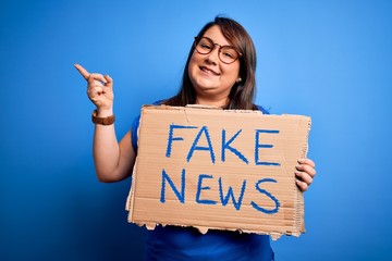 Beautiful plus size woman holding fake news banner for false journalism over isolated background...