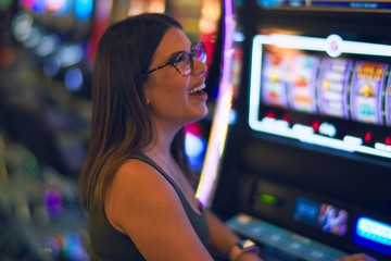 Young beautiful woman smiling happy and confident. Sitting with smile on face playing slot machine at casino