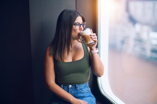 Young beautiful woman on vacation smiling happy and confident. Standing on a deck of ship with smile on drinking coffee face doing a cruise