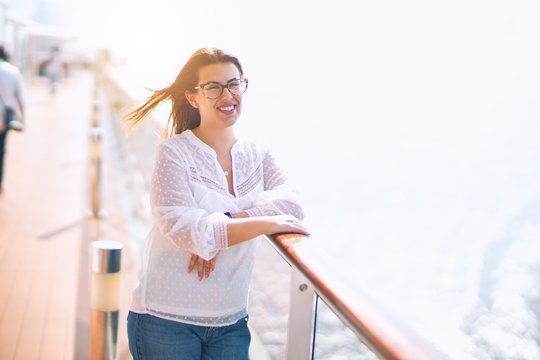 Young beautiful woman on vacation smiling happy and confident. Standing on a deck of ship with smile on face doing a cruise