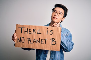 Young handsome chinese activist man protesting asking for care the planet on manifestation serious face thinking about question, very confused idea