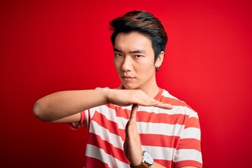 Young handsome chinese man wearing casual striped t-shirt standing over red background Doing time...