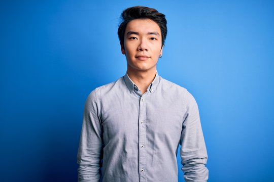 Young handsome chinese man wearing casual shirt standing over isolated blue background Relaxed with serious expression on face. Simple and natural looking at the camera.