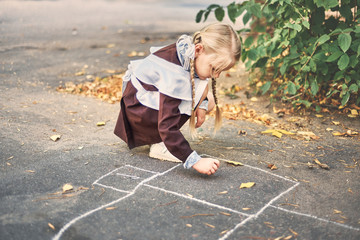 Fototapeta premium little girl draws with chalk on the pavement. schoolgirl plays in the yard. creativity concept.