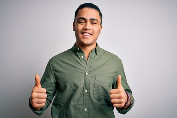 Young brazilian man wearing casual shirt standing over isolated white background success sign doing...