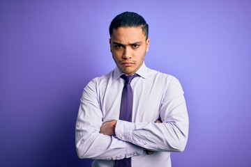 Young brazilian businessman wearing elegant tie standing over isolated purple background skeptic and nervous, disapproving expression on face with crossed arms. Negative person.