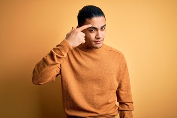 Young brazilian man wearing casual sweater standing over isolated yellow background pointing...