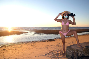 An senior Asian woman dressed in a pink swimsuit and has a nose mask. Protect Virus COVID-19 and PM2.5 protection. Use binoculars to looking.