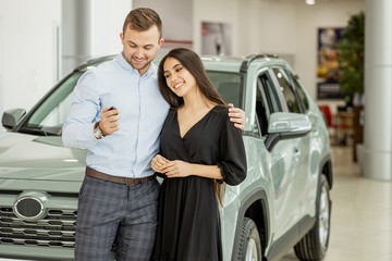 Fototapeta na wymiar young couple buying their new first family car in dealership, beautiful car in the background, happy owners of new jeep