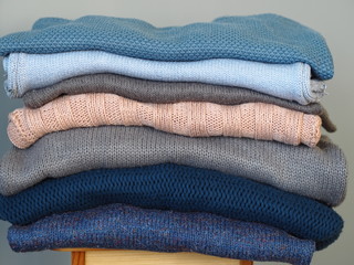 Warm knitwear stacked on a bench after washing. Store. Blue gray white tones. Close-up. Gray background.