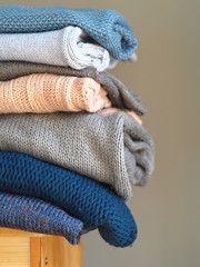 Warm knitwear stacked on a bench after washing. Store. Blue gray white tones. Close-up. Gray background.