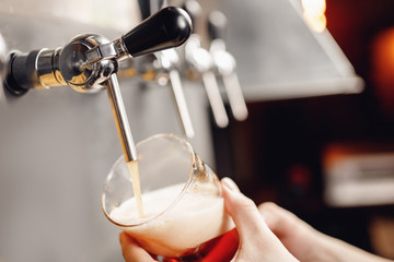 Bartender pours beer from tap into glass, dark background. Alcohol craft drink concept