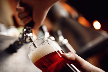 Fototapeta na wymiar Closeup hand barman dark craft cold beer pour in glass from crane in pub