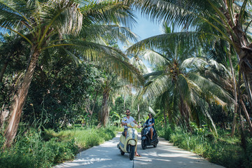 Two men on motorcycles in palm trees on a tropical island