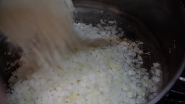 Un primer plano de cebolla siendo agregada a una sart&eacute;n caliente. La imagen captura el momento en que la cebolla empieza a saltear, resaltando el proceso de cocci&oacute;n y el aroma que se desarrolla.