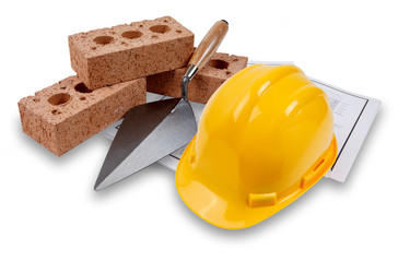 A set of house building bricks and trowel, with a yellow hard hat, on a set of building plans,...