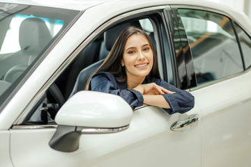 portrait of young beautiful smiling lady sitting in new car, attractive woman happy to be owner of new auto, look at camera.