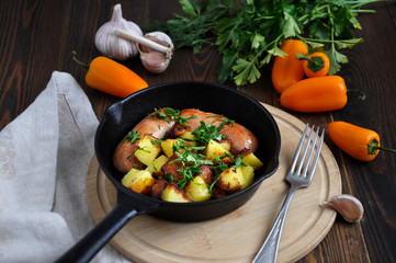 Small portioned pan with fried potatoes and sausages. Fresh herbs and vegetables next to this.