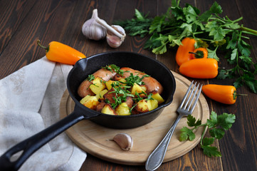 Small portioned pan with fried potatoes and sausages. Fresh herbs and vegetables next to this.
