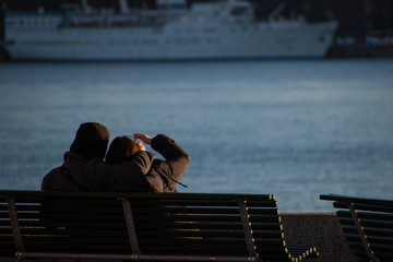 Couple on a coastline bench peering into the distance