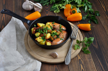 Small portioned pan with fried potatoes and sausages. Fresh herbs and vegetables next to this.