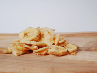 Pile of dried banana chips on light wooden board and light grey background. Concept snack, exotic food.