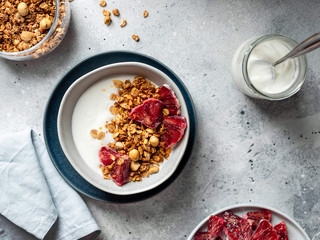 bowl of greek yogurt, granola and bloody orange on a gray background. healthy breakfast concept. horizontal image, copy space, table top view.