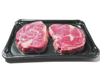 Two fresh premium rib eye steak in a vacuum pack package on a white background.