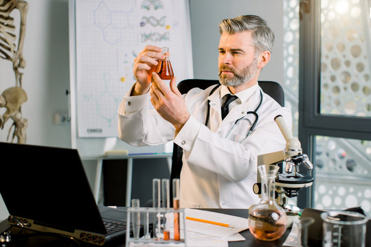 Senior doctor man scientist virologist researcher, analyzing chemistry flask with new substance, vaccine, evaluating results. Professor discovered a new formula for treating disease in laboratory.
