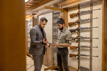 young salesman, consultant help customer to choose weapon in gun store. firearm, defense, weapons,...