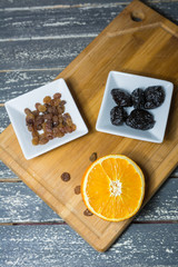 Sliced orange and dried fruit in pots set on a wooden kitchen board.
