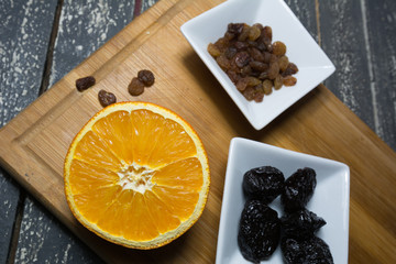 Sliced orange and dried fruit in pots set on a wooden kitchen board.