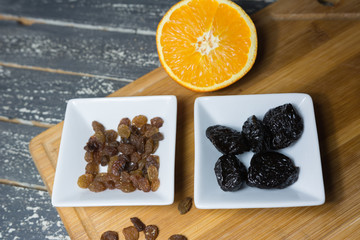 Raisins and prunes in pots set on a wooden kitchen board.