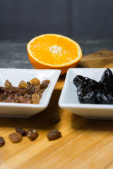 Raisins and prunes in pots set on a wooden kitchen board.