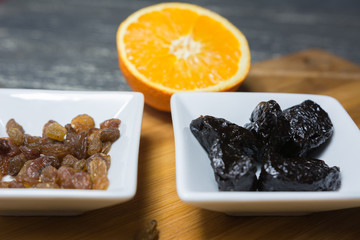 Raisins and prunes in pots set on a wooden kitchen board.
