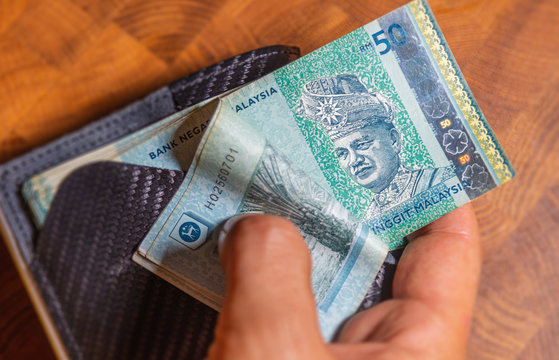 Male hands counting 50 Ringgit Malaysia in a leather wallet on a wooden table. RM50 in mans hand. Malaysian Ringgit shown by young man in a wallet. Close up to Malaysian currency.