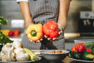 Close up of female hands holding fresh yellow and red peppers in their hands in the kitchen.