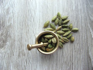 Green cardamom pods in brass mortar on wooden background. Top view. close up.
