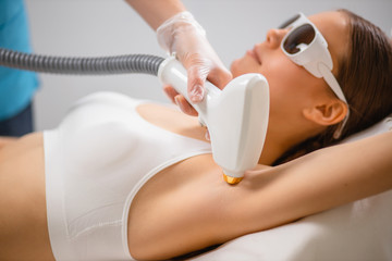 side view on young caucasian female getting hair removal from underarms in salon. lady in...