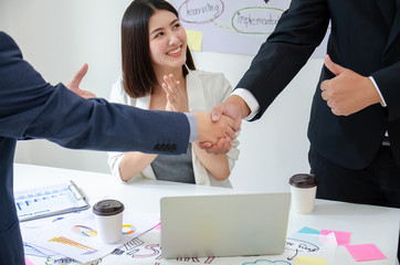 Asian secretary very happy that her supervisor able to enter business agreement with partner company. Clapping hands while the businessmen are holding hands, shaking hands, finishing up a meeting