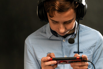 A teenager wearing headphones, enthusiastically playing a game on his smartphone. Close up. Dark...
