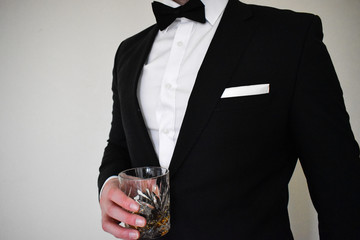 A close up view of a man in a black tuxedo holding a whiskey glass